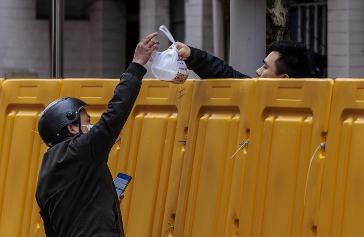 Ételfutár kézbesíti a rendelést egy kordonnal elkerített tömb lakójának Sanghajban 2022. március 31-én. A hatóságok Sanghajt március 28-tól két szakaszban lezárták, és felfüggesztették a tömegközlekedést a koronavírus-fertőzöttek kiszűrése érdekében. Fotó: MTI/EPA/Alex Plavevski