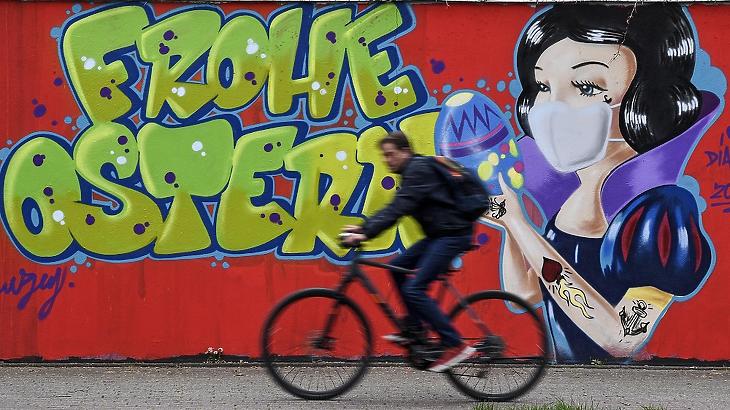 Kerékpáros halad el egy „Boldog Húsvéti Ünnepeket” jelentésű falfelirat előtt a koronavírus-járvány idején a németországi Hamm városában 2020. április 13-án. MTI/AP/Martin Meissner