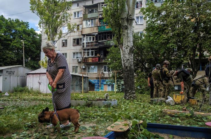 Megrongált lakóház előtt sétáltatja kutyáját egy nő, mögötte ukrán katonák Kramatorszkban 2022. július 19-én, miután orosz rakétatámadás érte a donyecki régióban fekvő várost. Fotó: MTI/EPA