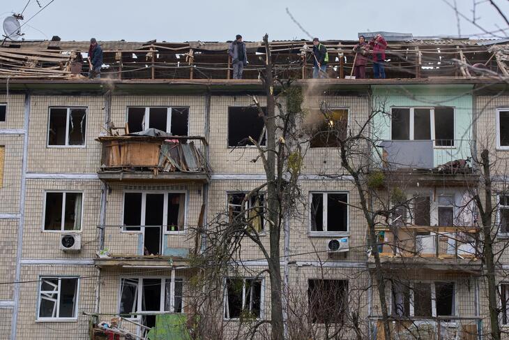 Városi alkalmazottak takarítják el a törmeléket egy orosz dróntámadásban megrongálódott lakóház tetejéről Kijevben 2025. decemberében.