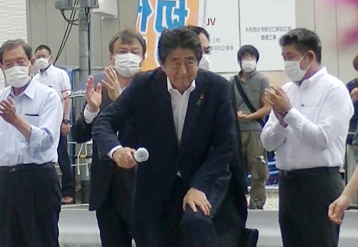 Abe Sinzó fellép a pódiumra beszéde előtt. Mögötte zöld pólóban a lövést később leadó férfi. Fotó: EPA/JIJI PRE
