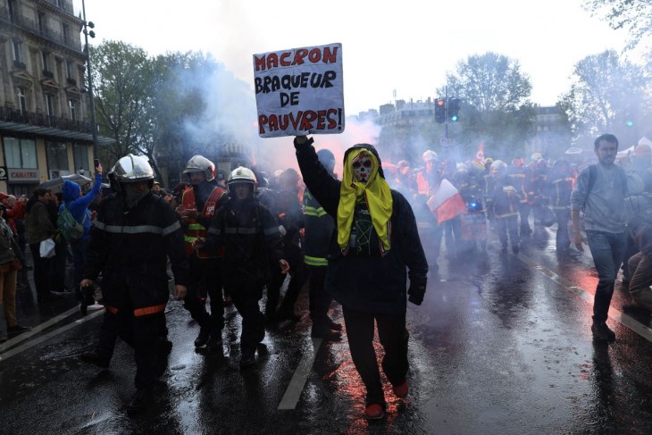 Mentőalakulatok dolgozói és egy tiltakozó táblát tartó férfi részt vesz a munka ünnepe alkalmából rendezett felvonuláson Párizsban 2023. május 1-jén. Fotó: MTI/AP