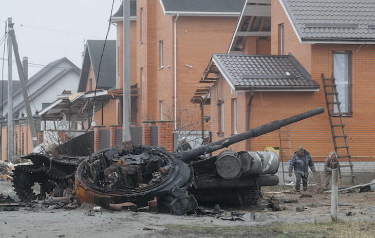 Helyi lakosok egy megsemmisült orosz páncélozott harci jármű roncsa mellett a Kijev megyében fekvő és az ukrán hadsereg által visszafoglalt Dmitrivkában 2022. április 2-án. Fotó: MTI/EPA/Szerhij Dolzsenko
