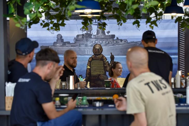 Egy kijevi bár a háttérben egy poszterrel, amelyen egy ukrán katona bemutat egy orosz hadihajónak a Kígyós-szigetnél. Fotó: EPA/OLEG PETRASYUK