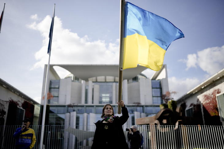 Ukrán zászlót lengető egy nő a berlini kancellári hivatal előtt 2022. október 11-én, miközben a világ hét iparilag legfejlettebb államát tömörítő G7-csoport vezetői videomegbeszélést folytatnak Volodimir Zelenszkij részvételével az épületben. Fotó: MTI/AP/Markus Schreiber