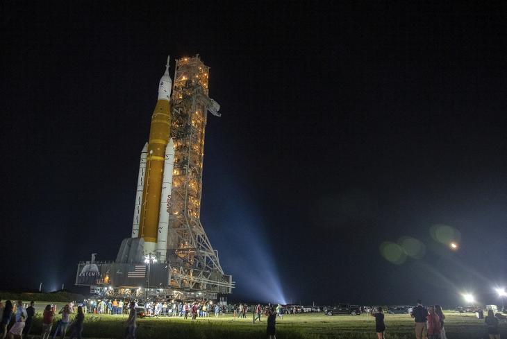 Az amerikai űrkutatási hivatal (NASA) új SLS óriásrakétája, csúcsán az Orion kapszulával, miután kigördült a szerelőcsarnokból a floridai Cape Canaveralnál működő Kennedy Űrközpontban 2022. augusztus 16-án. Az Artemis nevet viselő új űrprogram az első útján Hold körüli pályára állítja a legénységet egyelőre nem szállító Orion kapszulát, amely a tervek szerint mintegy 40 nappal később tér vissza a Földre. A NASA a mostani tervek szerint pénteken indítja útnak az SLS óriásrakétát tesztelő Artemis 1-et. Fotó: MTI/EPA/Cristobal Herrera Ulashkevich