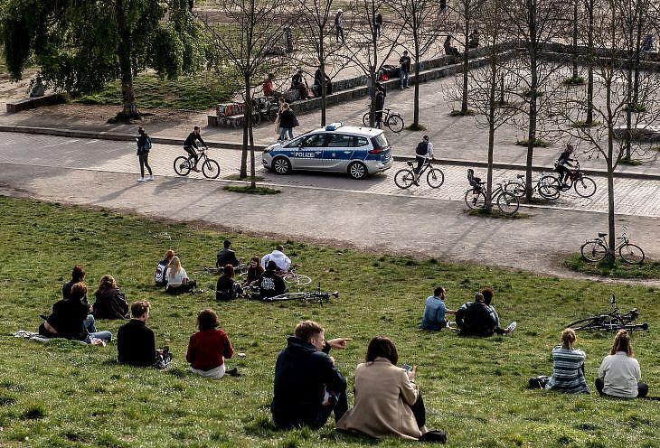 Pihenő emberek és egy rendőrautó a berlini Mauerparkban 2020. április 16-án. EPA/FILIP SINGER 