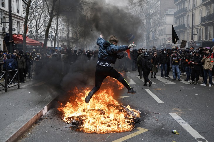 A nyugdíjreform ellen tüntetők egyike átugrik egy felgyújtott szemetesedényt Párizsban 2023. március 28-án.  Fotó: MTI/EPA/Christophe Petit Tesson 