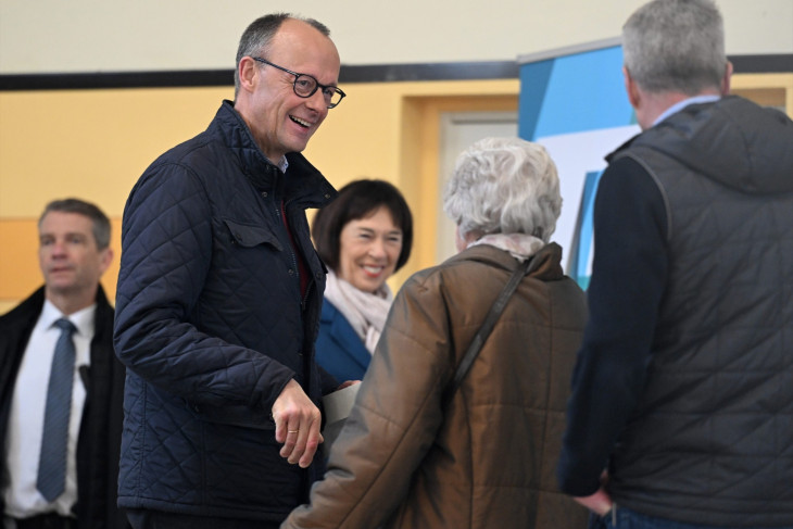 Friedrich Merz, a Kereszténydemokrata Unió (CDU) elnöke, a CDU és bajor testvérpártja, a Keresztényszociális Unió (CSU) közös jelöltje (b) a helyi emberekkel beszéget, mielőtt leadja szavazatát a németországi előrehozott szövetségi parlamenti választáson az Észak-Rajna-Vesztfália tartományban lévő Arnsbergben 2025. február 23-án. 