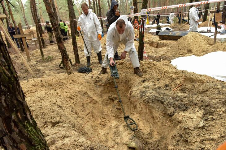 Fémdetektorral vizsgál át egy sírt az azonosítatlan áldozatok földi maradványait exhumáló csoport egyik tagja a kelet-ukrajnai Harkiv megyében levő Izjumnál 2022. szeptember 16-án, a tömegsír felfedezésének másnapján. Az ukrán hatóságok több mint 440 egyenként elásott holttestet hantoltak ki az orosz erőktől nemrégiben visszafoglalt város melletti erdőben. Fotó: MTI/EPA