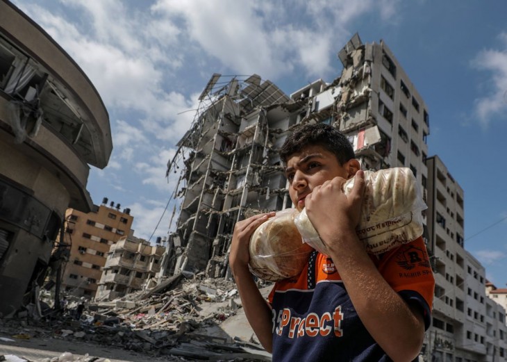 Izraeli légitámadásban összedőlt ház romjai mellett visz kenyeret egy palesztin fiatalember Gázában 2023. október 16-án. A Gázai övezetet irányító Hamász palesztin iszlamista szervezet október 7-én többfrontos támadást indított Izrael ellen, ahol több mint 1300 ember életét vesztette. A Hamász elleni izraeli válaszcsapások több mint 2700 palesztin halálát okozták a Gázai övezetben. Fotó: MTI/EPA