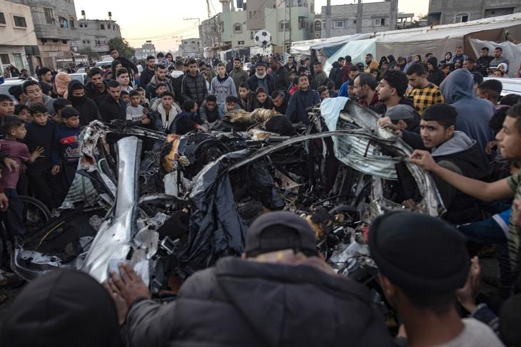 Palesztinok egy izraeli légicsapásban megsemmisült autót vizsgálnak a Gázai övezet déli részén lévő rafahi menekülttáborban, 2024. február 7-én.  Fotó: EPA / Haitham Imad