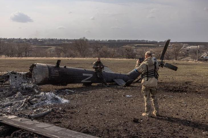 Ukrán katonáról készít képet egyik társa egy megsemmisített orosz helikopter mellett a kelet-ukrajnai Harkiv közelében 2022. március 31-én. Fotó: MTI/EPA
