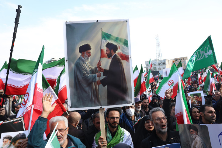 Ali Hamenei néhai ajatollahot és fiát, Modzstaba Hameneit ábrázoló transzparenst fog egy támogatója egy teheráni megmozduláson 2026. március 9-én