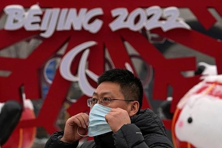 A 2022-es pekingi téli olimpia plakátja előtt veszi fel védőmaszkját egy férfi. Fotó: MTI/AP