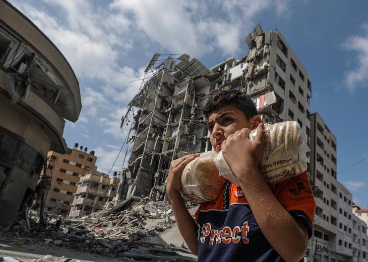 Egy palesztin fiatalember kenyeret visz egy izraeli légitámadásban összedőlt ház romjai mellett Gázában. Fotó: MTI/EPA/Mohamed Szaber