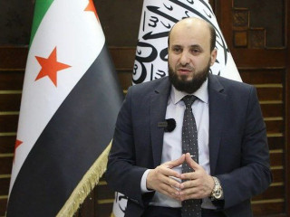 Az új miniszterelnök Mohamad al-Basír a szír és az iszlamista zászló előtt beszél