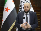 Az új miniszterelnök Mohamad al-Basír a szír és az iszlamista zászló előtt beszél