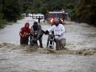 Emberek kelnek át egy elárasztott úton a heves esőzések következtében a dominikai köztársaságbeli San Jose de Ocoában, 2023. november 18-án. Egy ember eltűnt, legalább 1522 embernek kellett elhagynia otthonát, és egy híd is összeomlott a Dominikai Köztársaságban az intenzív esőzések miatt, amelyek okán a hatóságok az ország 32 tartományából 30-ban riasztást, 11-ben pedig vörös fokozatú riasztást rendeltek el. Fotó: EPA / Orlando Barria