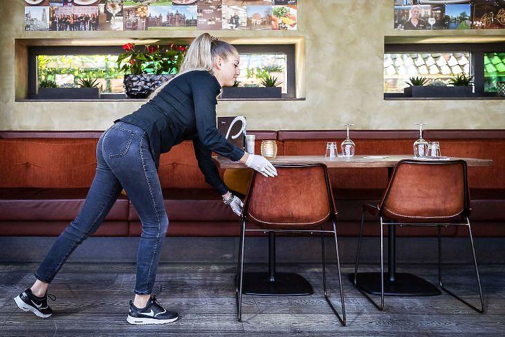 Pincérnő rendezgeti a székeket egy teszthelyszínként szolgáló étteremben a hollandiai Breukelenben 2020. április 21-én. EPA/REMKO DE WAAL